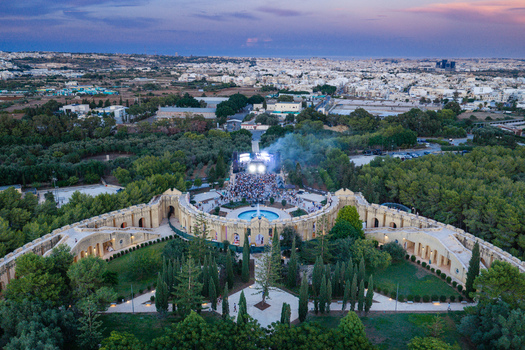 Attard Malta 20 September 2026 Aerial view of Park Nazzjonali Ta Qali featuring a concert stage with a large crowd a central fountain and lush greenery under a dusk sky. Attard Malta 20 September 2026 Aerial view of Park Nazzjonali Ta Qali featuring a concert stage with a large crowd a central fountain and lush greenery under a dusk sky.