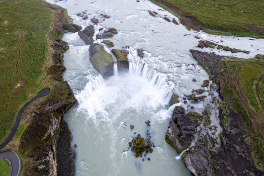 Aerial view of Godafoss Waterfall with cascading white water and rocky cliffs surrounded by green mossy banks in Thingeyjarsveit Iceland. Aerial view of Godafoss Waterfall with cascading white water and rocky cliffs surrounded by green mossy banks in Thingeyjarsveit Iceland.