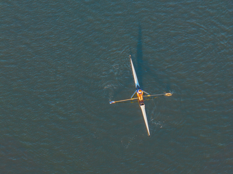 Aerial view of a single rower in a scull boat gliding across the calm waters of the Vistula River in Gdansk Pomeranian Voivodeship Poland. Aerial view of a single rower in a scull boat gliding across the calm waters of the Vistula River in Gdansk Pomeranian Voivodeship Poland.