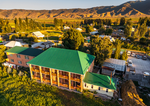 Aerial view of a building with a green roof in the Chon Kemin valley surrounded by trees fields and mountains under golden hour light in Kaindy Chuy Province Kyrgyzstan.