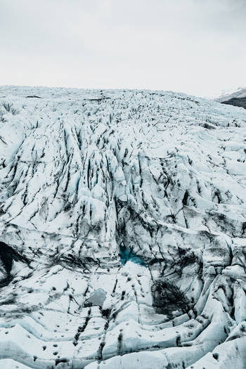 Aerial view of Vatnajokull glacier featuring deep crevasses textured ice formations and patches of blue meltwater under an overcast sky in Iceland.