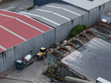 Melbourne Australia 25 September 2026 Aerial view of an industrial site with a concrete mixer truck yellow loader and storage bays for materials beside factory buildings.