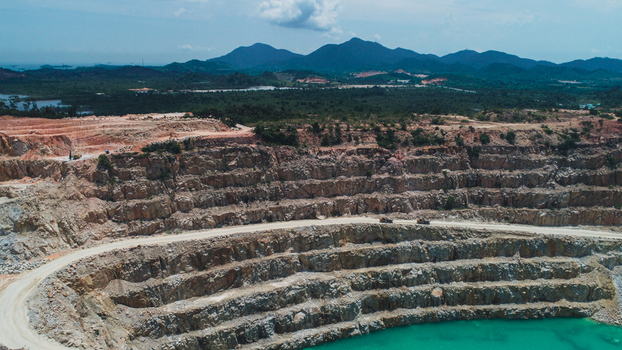 Aerial view of a gravel and sand mine on Karimun Island featuring terraced rock walls a turquoise water pit and heavy machinery in Karimun Kepulauan Riau Indonesia.