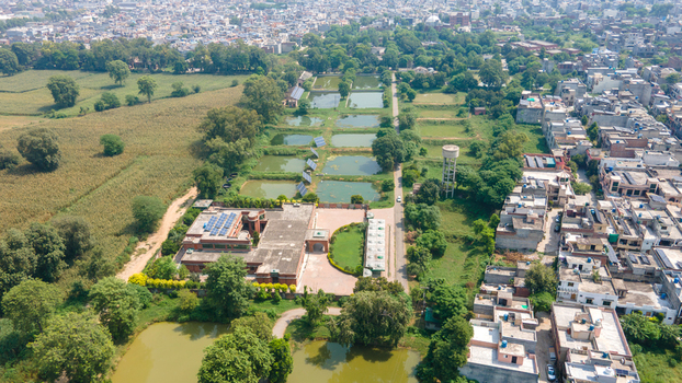 Aerial view of a fishing farm with multiple rectangular ponds solar panels and a building complex surrounded by green fields and urban residential areas in Punjab Pakistan. Aerial view of a fishing farm with multiple rectangular ponds solar panels and a building complex surrounded by green fields and urban residential areas in Punjab Pakistan.