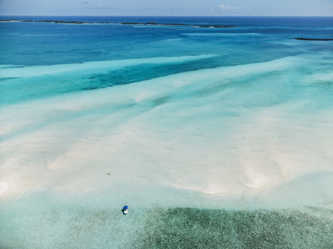 Aerial view of the Man O War Cay Sandbar with turquoise waters and a small boat anchored in the shallows under a clear blue sky in Rolletown Exuma The Bahamas. Aerial view of the Man O War Cay Sandbar with turquoise waters and a small boat anchored in the shallows under a clear blue sky in Rolletown Exuma The Bahamas.