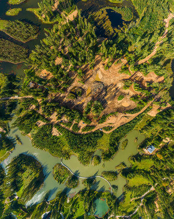 Aerial view of a forested landscape with a winding river dirt paths and a small footbridge crossing the water in Latvia. Aerial view of a forested landscape with a winding river dirt paths and a small footbridge crossing the water in Latvia.
