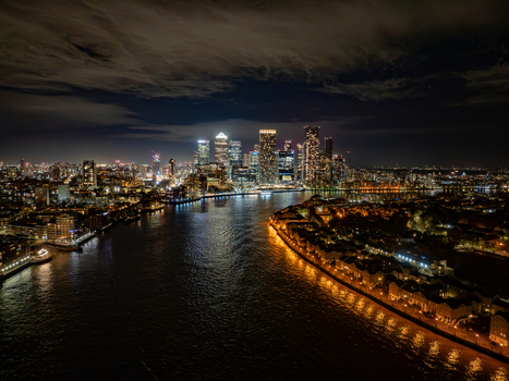 Aerial view of the Canary Wharf skyline illuminated at night with the River Thames reflecting city lights in London England United Kingdom.