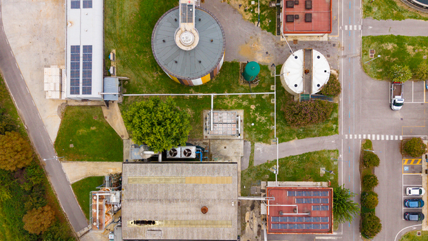 Aerial view of wastewater treatment plant featuring circular tanks industrial buildings with solar panels and surrounding green spaces in Rancate Lombardia Italy.