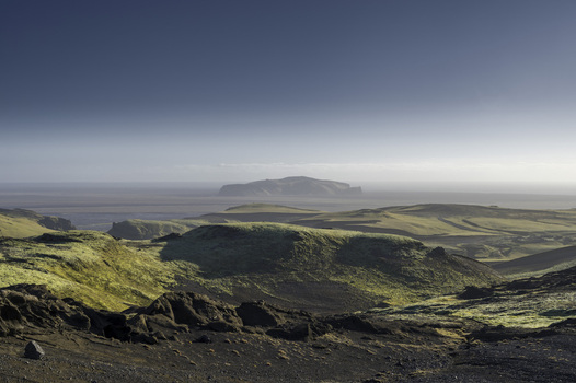 View of the vast volcanic landscape featuring moss covered hills and black rocky terrain under a clear blue sky in Katla Geopark Skaftarhreppur Iceland.