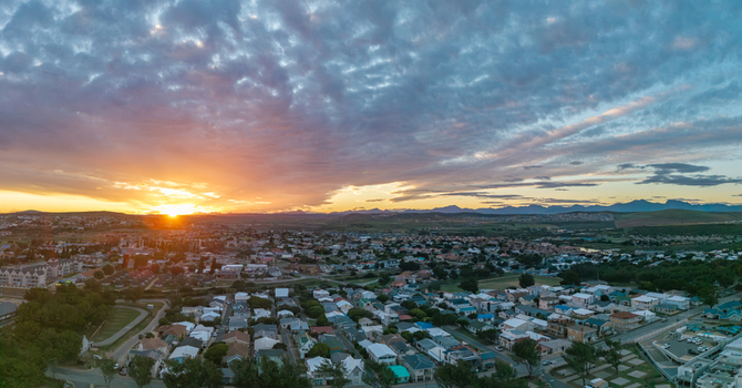 Aerial view of Hartenbos residential area with rooftops and streets under a dramatic sunset sky and mountain range in Mossel Bay Western Cape South Africa. Aerial view of Hartenbos residential area with rooftops and streets under a dramatic sunset sky and mountain range in Mossel Bay Western Cape South Africa.