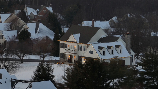 Aerial view of a house decorated with Christmas lights surrounded by snow covered lawns and trees during a winter sunset in Warwick Township Pennsylvania United States.