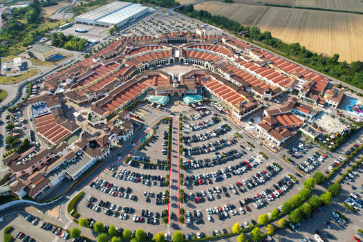 Aerial view of Designer Outlet Serravalle featuring its distinctive circular architecture and red tiled roofs surrounded by large parking areas in Serravalle Scrivia Piemonte Italy. Aerial view of Designer Outlet Serravalle featuring its distinctive circular architecture and red tiled roofs surrounded by large parking areas in Serravalle Scrivia Piemonte Italy.