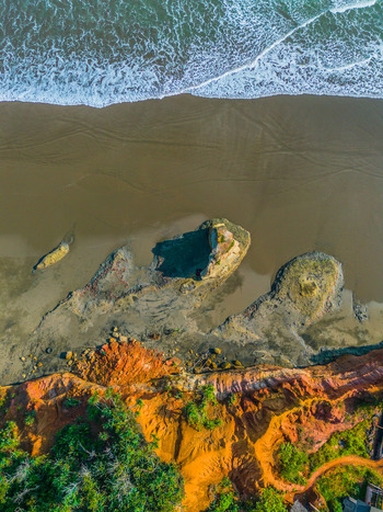 Aerial view of the rugged coastline with golden cliffs dark sand beach and crashing waves in Bali Bali Indonesia. Aerial view of the rugged coastline with golden cliffs dark sand beach and crashing waves in Bali Bali Indonesia.