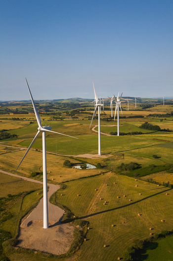 Aerial view of wind turbines standing tall against the clear blue sky contrasting with the golden fields and patchwork of green pastures Salles Curan Occitanie France. Aerial view of wind turbines standing tall against the clear blue sky contrasting with the golden fields and patchwork of green pastures Salles Curan Occitanie France.