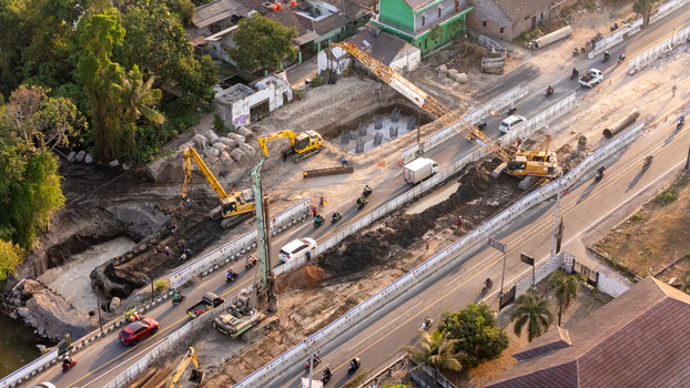Indonesia 24 September 2026 Aerial view of a construction site with excavators a crane and road work along a busy road with traffic.