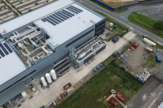Aerial view of a modern data center facility featuring rooftop solar panels industrial HVAC cooling units and surrounding infrastructure in the United Kingdom.
