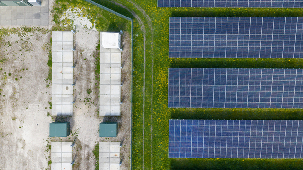 Aerial view of rows of solar panels on a green field with yellow flowers next to concrete foundations and utility infrastructure in Warmenhuizen North Holland Netherlands. Aerial view of rows of solar panels on a green field with yellow flowers next to concrete foundations and utility infrastructure in Warmenhuizen North Holland Netherlands.