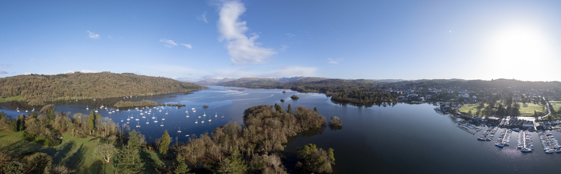 Aerial view of boats resting on the still dark waters reflecting the clear blue sky fringed by lush green shores and the town Windermere England United Kingdom. Aerial view of boats resting on the still dark waters reflecting the clear blue sky fringed by lush green shores and the town Windermere England United Kingdom.