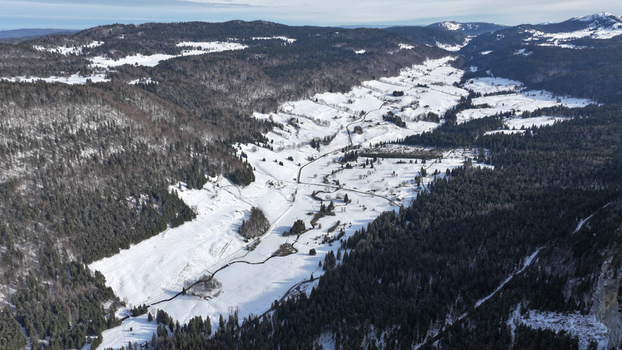 Aerial view of the snow dusted valley floor contrasting with the dark dense forests a tranquil winter scene unfolds Gex Auvergne Rhône Alpes France. Aerial view of the snow dusted valley floor contrasting with the dark dense forests a tranquil winter scene unfolds Gex Auvergne Rhône Alpes France.