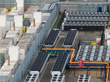 Aerial view of a data center with rows of industrial cooling fans complex piping systems and secure perimeter fencing in the United Kingdom.