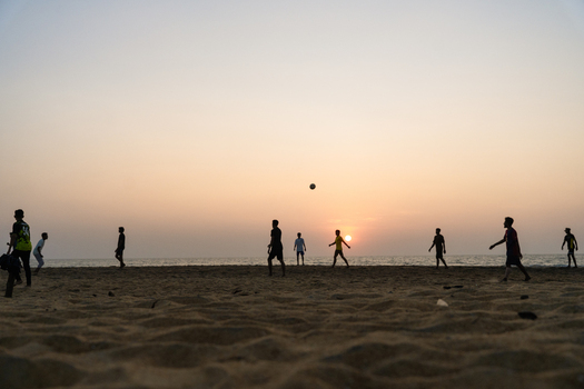 View of silhouetted people playing football on a sandy beach under a warm sunset sky with the ocean in the background Galle Southern Province Sri Lanka.