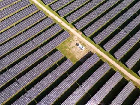 Aerial view of rows of solar panels in a large solar farm with a dirt path and electrical equipment in Poland.