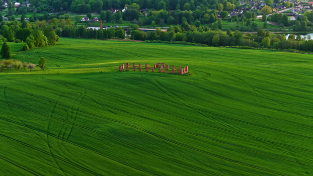 Aerial view of a small brick ruin situated in the middle of a vast vibrant green field with tire tracks visible in the grass Latvia. Aerial view of a small brick ruin situated in the middle of a vast vibrant green field with tire tracks visible in the grass Latvia.