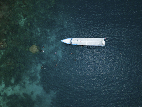 Aerial view of a pristine white boat surrounded by swimmers in the deep blue sea near the Cemara Kecil Snorkeling Spot Karimunjawa Central Java Indonesia.