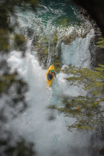 View of a kayaker in a yellow boat navigating the white water rapids of Rio Manso surrounded by lush green trees in San Carlos de Bariloche Rio Negro Argentina. View of a kayaker in a yellow boat navigating the white water rapids of Rio Manso surrounded by lush green trees in San Carlos de Bariloche Rio Negro Argentina.