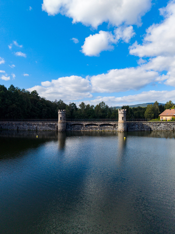 Aerial view of Fojtka Reservoir with its historic stone dam and towers surrounded by lush forest under a blue sky in Mnisek Liberecky kraj Czechia. Aerial view of Fojtka Reservoir with its historic stone dam and towers surrounded by lush forest under a blue sky in Mnisek Liberecky kraj Czechia.