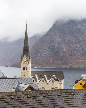 View of the iconic Hallstatt Lutheran Church spire overlooking the calm lake and misty mountains with traditional rooftops in the foreground Hallstatt Upper Austria Austria. View of the iconic Hallstatt Lutheran Church spire overlooking the calm lake and misty mountains with traditional rooftops in the foreground Hallstatt Upper Austria Austria.