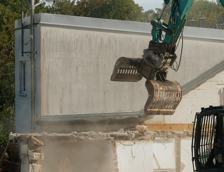 View of an excavator with a hydraulic grapple attachment demolishing a concrete wall at a construction site in Garching Bavaria Germany. View of an excavator with a hydraulic grapple attachment demolishing a concrete wall at a construction site in Garching Bavaria Germany.