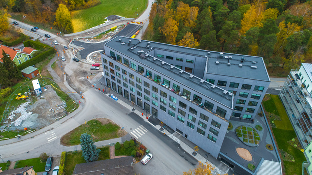 Aerial view of a modern V shaped office building with a grey facade surrounded by autumn trees a road and construction work in Sweden. Aerial view of a modern V shaped office building with a grey facade surrounded by autumn trees a road and construction work in Sweden.
