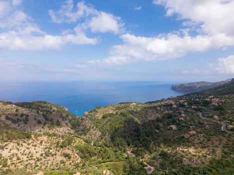 Aerial view of the lush green hills and rugged coastline overlooking the Mediterranean Sea under a blue sky with clouds in Valldemossa Balearic Islands Spain.