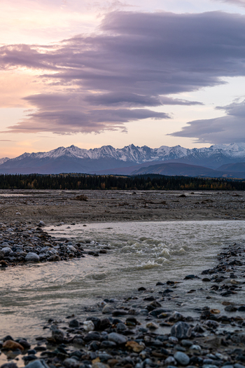 View of the Gerstle River with its rocky riverbed and flowing water set against a backdrop of snow capped mountains and a colorful sunset sky in Deltana Alaska United States. View of the Gerstle River with its rocky riverbed and flowing water set against a backdrop of snow capped mountains and a colorful sunset sky in Deltana Alaska United States.