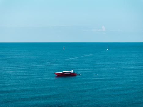 Aerial view of a red luxury boat anchored in the calm blue waters of Lacona Bay with distant sailboats on the horizon in Lacona Tuscany Italy.