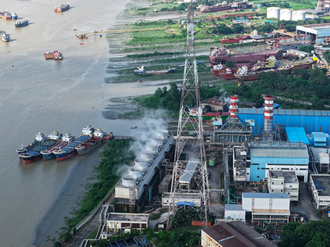 Aerial view of the Karnaphuli River industrial area with a power plant transmission tower and cargo ships docked along the riverbank in Chattogram Chittagong Division Bangladesh.