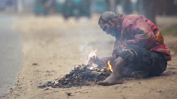 View of a man sitting by a small fire on a roadside Bangladesh. View of a man sitting by a small fire on a roadside Bangladesh.