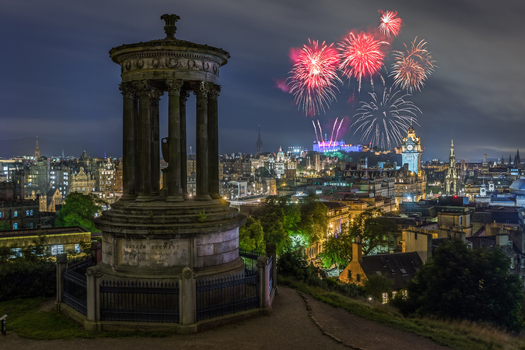 View of the Dugald Stewart Monument on Calton Hill with fireworks exploding over the illuminated city skyline and Edinburgh Castle at night Edinburgh Scotland United Kingdom. View of the Dugald Stewart Monument on Calton Hill with fireworks exploding over the illuminated city skyline and Edinburgh Castle at night Edinburgh Scotland United Kingdom.