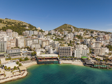 Aerial view of the coastal city of Saranda with its dense urban architecture hotels and sandy beach along the turquoise Ionian Sea in Saranda Vlore County Albania. Aerial view of the coastal city of Saranda with its dense urban architecture hotels and sandy beach along the turquoise Ionian Sea in Saranda Vlore County Albania.