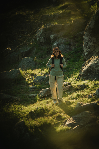 View of a woman trekking on a rocky mountain path during golden hour surrounded by grass and boulders in Tandil Buenos Aires Argentina. View of a woman trekking on a rocky mountain path during golden hour surrounded by grass and boulders in Tandil Buenos Aires Argentina.