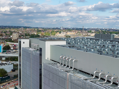 Aerial view of a modern data center featuring extensive rooftop cooling units industrial piping systems and a sleek facade set against an urban landscape in the United Kingdom. Aerial view of a modern data center featuring extensive rooftop cooling units industrial piping systems and a sleek facade set against an urban landscape in the United Kingdom.