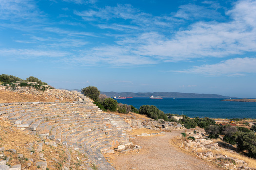 View of the Ancient Theatre of Thorikos with its stone seating overlooking the blue Aegean Sea and distant cargo ships under a clear sky in Thoricus Greece.
