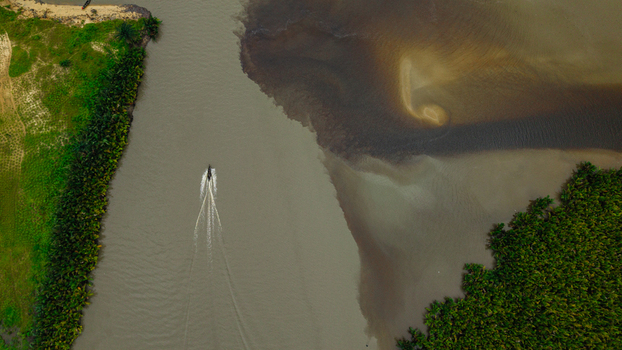 Aerial view of a small boat traveling along the Kwa Ibo River near Ibeno Beach surrounded by lush mangrove forests and sandy riverbanks in Kwa Ibo Akwa Ibom Nigeria.