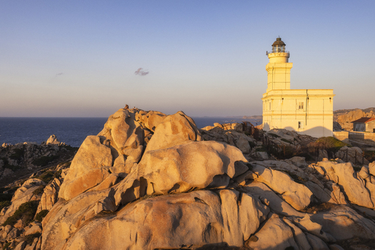 View of the Capo Testa lighthouse standing on rugged granite rock formations during golden hour with the Mediterranean Sea in the background Capo Testa Sardegna Italy.