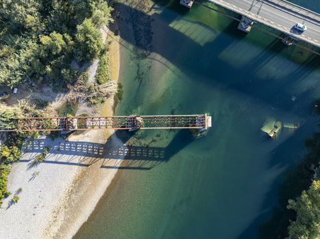 Aerial view of the historic Old Bridge over Drin River with its rusted metal structure casting a long shadow on the clear turquoise water and gravel riverbank in Shkoder Shkoder County Albania. Aerial view of the historic Old Bridge over Drin River with its rusted metal structure casting a long shadow on the clear turquoise water and gravel riverbank in Shkoder Shkoder County Albania.