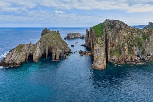 Aerial view of Silence Beach Viewpoint with dramatic jagged cliffs turquoise ocean water and rocky islets under a cloudy sky in Cudillero Asturias Spain.