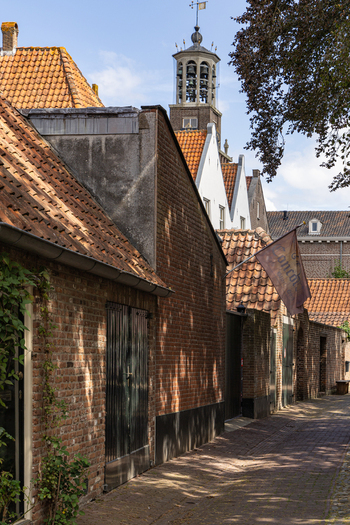 View of a narrow cobblestone street in the historic town of Heusden featuring traditional brick buildings a church tower and a hanging sign in Heusden North Brabant Netherlands.