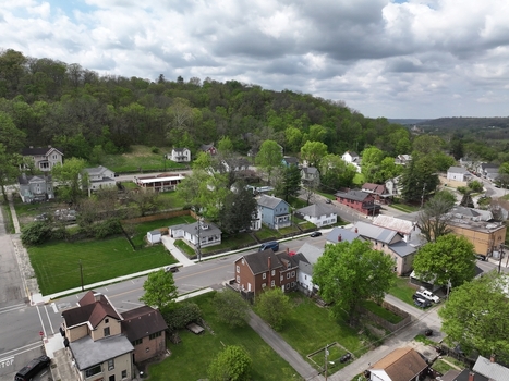 Aerial view of residential houses nestled along streets at the foot of a lush green wooded hill under a cloudy sky in Aurora Indiana United States. Aerial view of residential houses nestled along streets at the foot of a lush green wooded hill under a cloudy sky in Aurora Indiana United States.