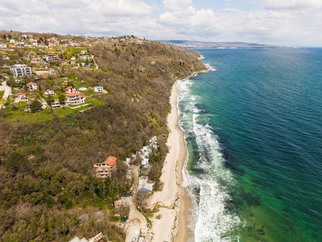 Aerial view of the sandy shoreline of Fichoza Beach Veteran with turquoise sea waves crashing against the coast and lush green cliffs under a cloudy sky in Varna Varna Bulgaria. Aerial view of the sandy shoreline of Fichoza Beach Veteran with turquoise sea waves crashing against the coast and lush green cliffs under a cloudy sky in Varna Varna Bulgaria.